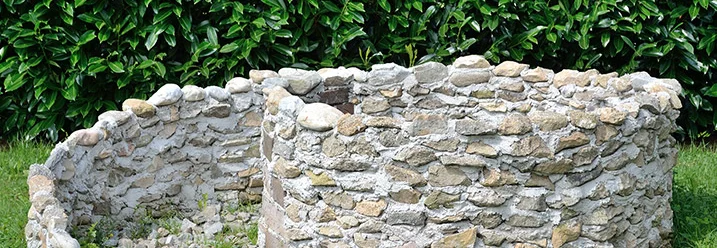 Eine Kräuterspirale aus Steinen wird vor einer grünen Hecke aufgebaut.